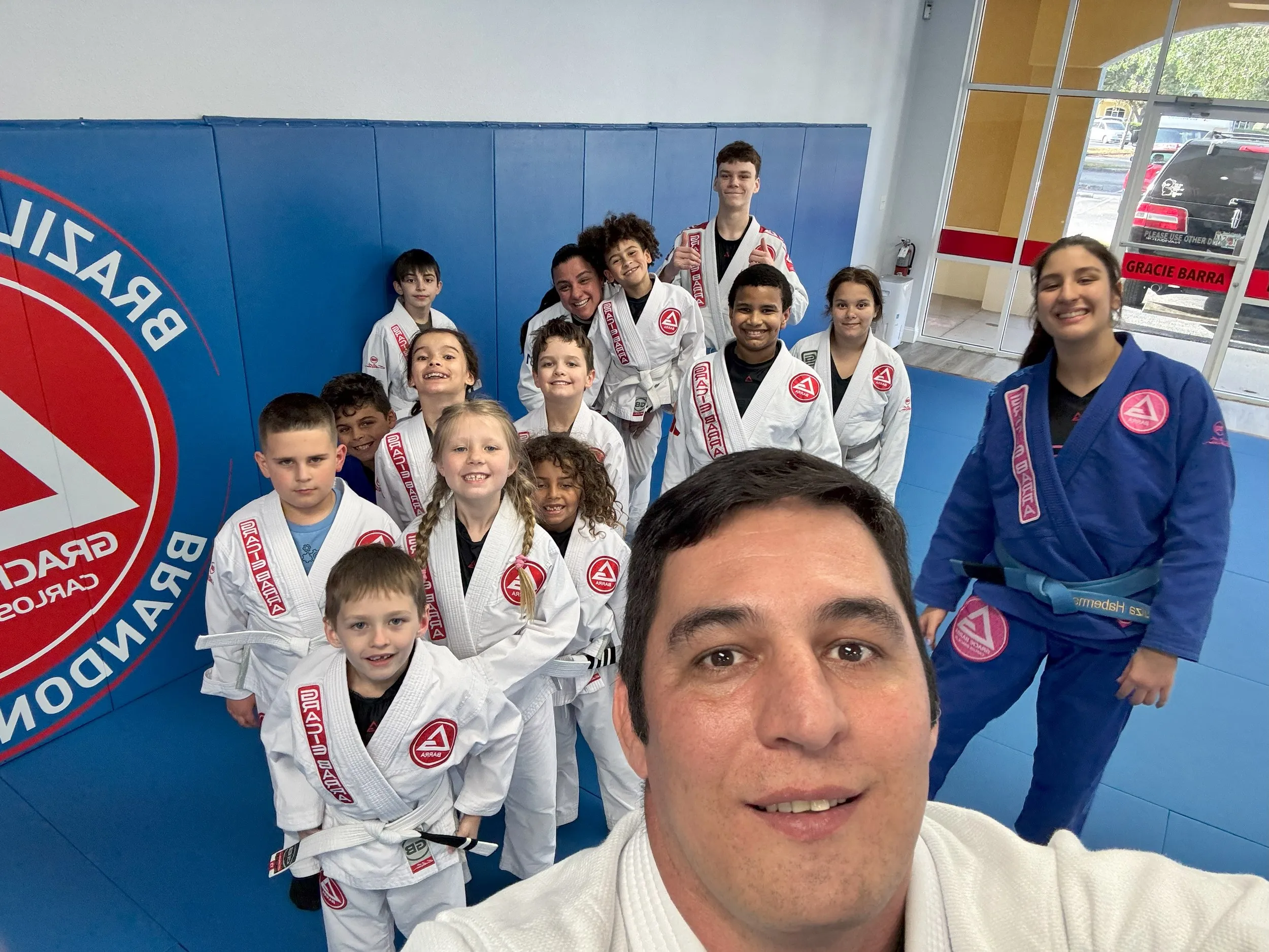 Professor Vand takes a selfie with a smiling group of kids-class students and Coach Luiza at Gracie Barra Brandon.